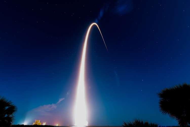 An arcing plume of fire from a rocket launch streaks into the nighttime sky.
