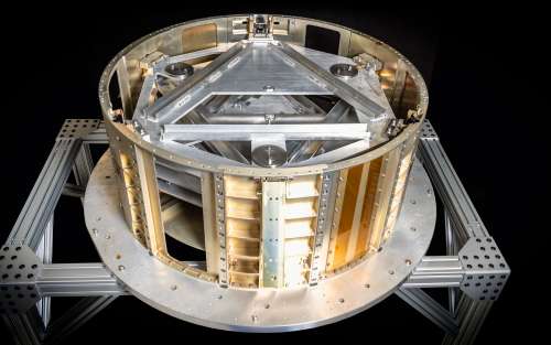 Image shows a metallic dispenser designed for holding and deploying disk-shaped satellites. The dispenser has a cylindrical frame with multiple slots and compartments for securely housing the satellites. The structure is supported by a robust framework made of metal beams and plates, providing stability and durability.