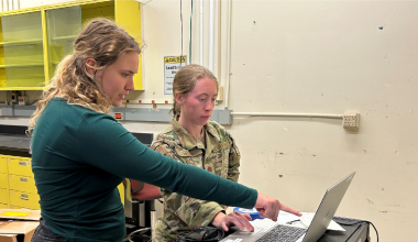 Two women, one cadet and another plain clothed pointing at a computer screen.